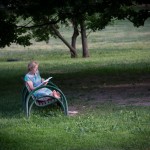 An older woman reading a book in a park near Moscow State University on a Saturday evening.