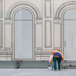 A city worker cleaning in front of a building whose facade is under reconstruction.