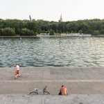 A biker taking a break along the Moscow River as a man walks by with his child.