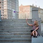 A young Russian girl taking a selfie along the Moscow River at sunset.