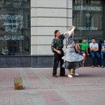 An elderly couple dancing on Arbat pedestrian street to earn some money as young men look on.