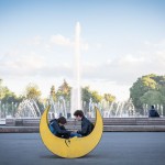 A young couple sitting in a moon shaped chair in front of a fountain.