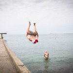 Russian youth doing a backflip into the water on the Sochi shore.