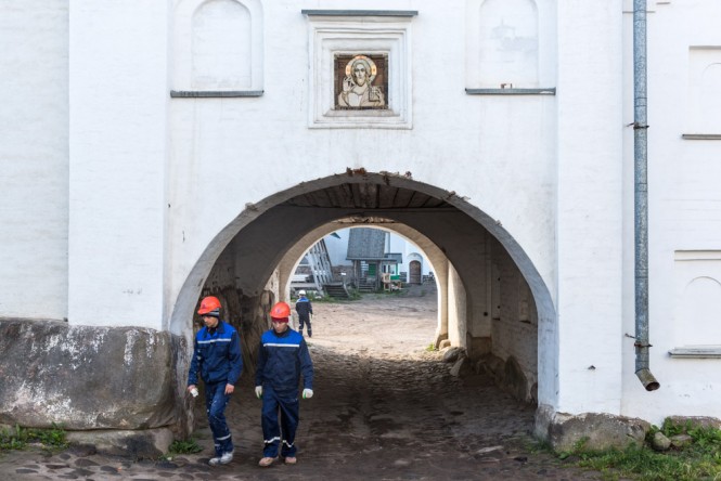 Construction workers passing through a gateway inside the Solovetsky Monastery. A photo of Jesus hangs above them.