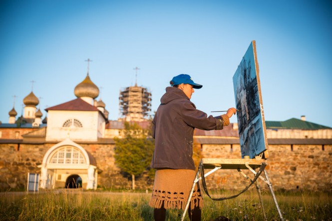 A Belarusian girl painting in front of the Solovetsky Monastery during sunset. 
