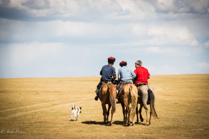 Young Kyrgyz riding off, their dog in tow, to play the national game of kok boru.