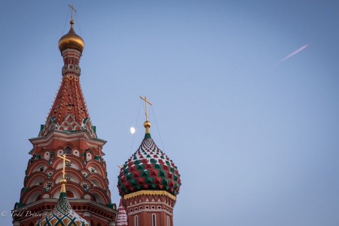 A plane flies over St. Basil's cathedral and the moon shines between its cupolas.
