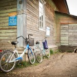 As villages are small, many residents get around on bicycles. These bicycles are leaning up against an old convenience store. A dog watches the bikes while the owners shop.