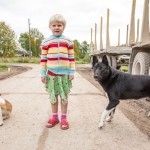 A colorfully-dressed village girl playing in front of her house. Dogs are omnipresent in Russian villages.